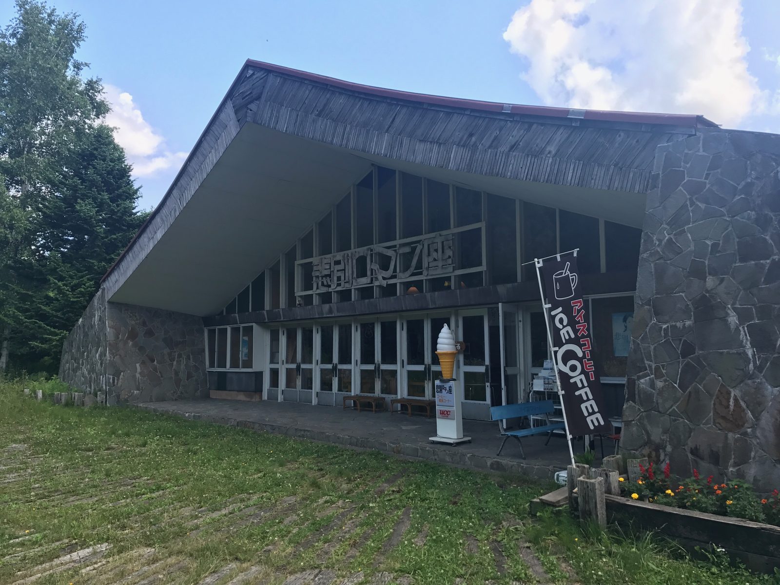 夏の悲別ロマン座。石積みの壁に四代目の切り文字の看板、手前に緑の芝