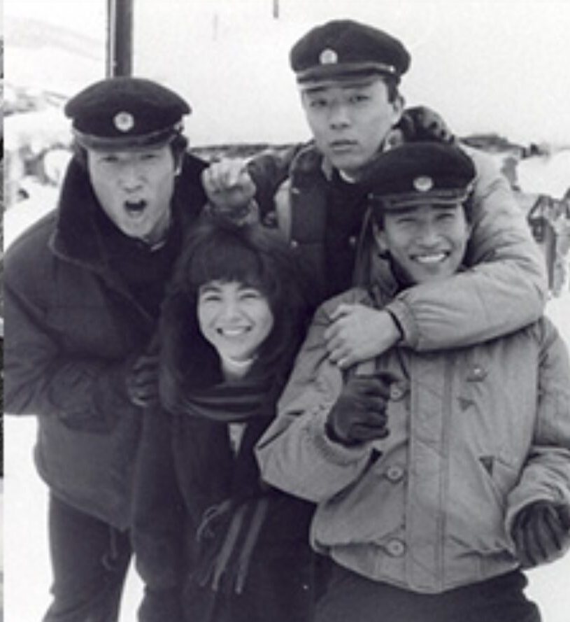 雪の中で学生帽をかぶった若者四人が肩を組んで笑っている